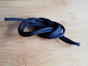 A coiled length of black paracord on a wooden table.