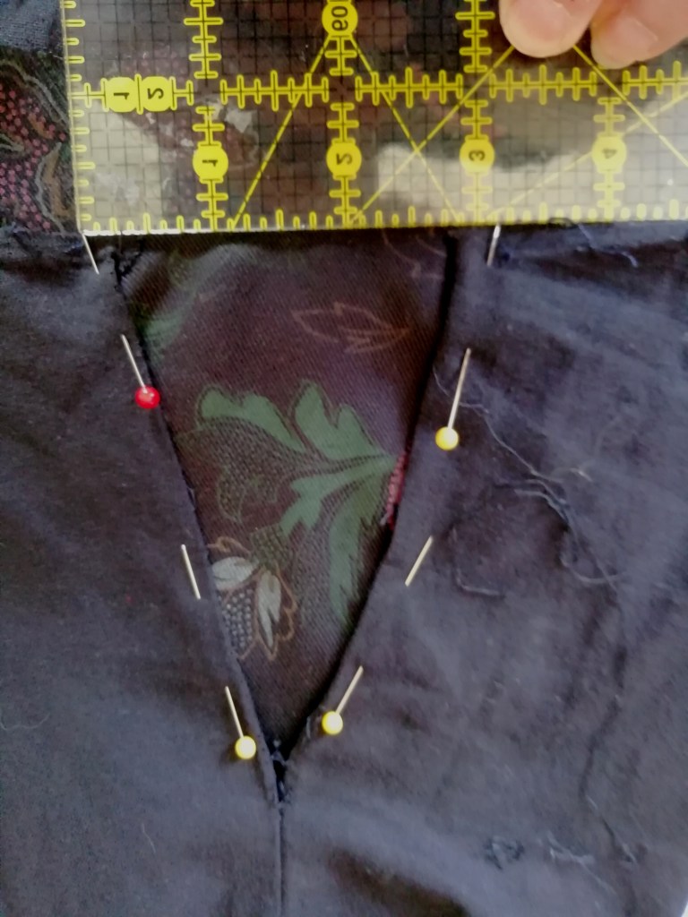 Using a sewing ruler to measure the opening for the gusset. Gusset fabric is facing out and pins hold the sleeve to the gusset.