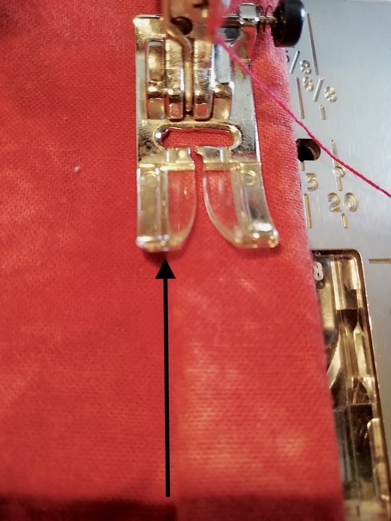 Stitching along the rolled up hem. An arrow indicates where to line up the hem with the marking on the presser foot.